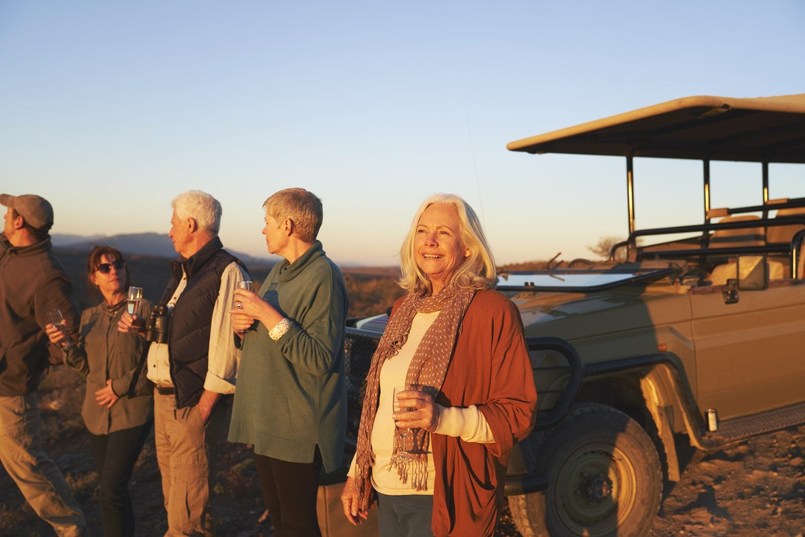 Travellers enjoying sundowners beside a safari vehicle at sunset